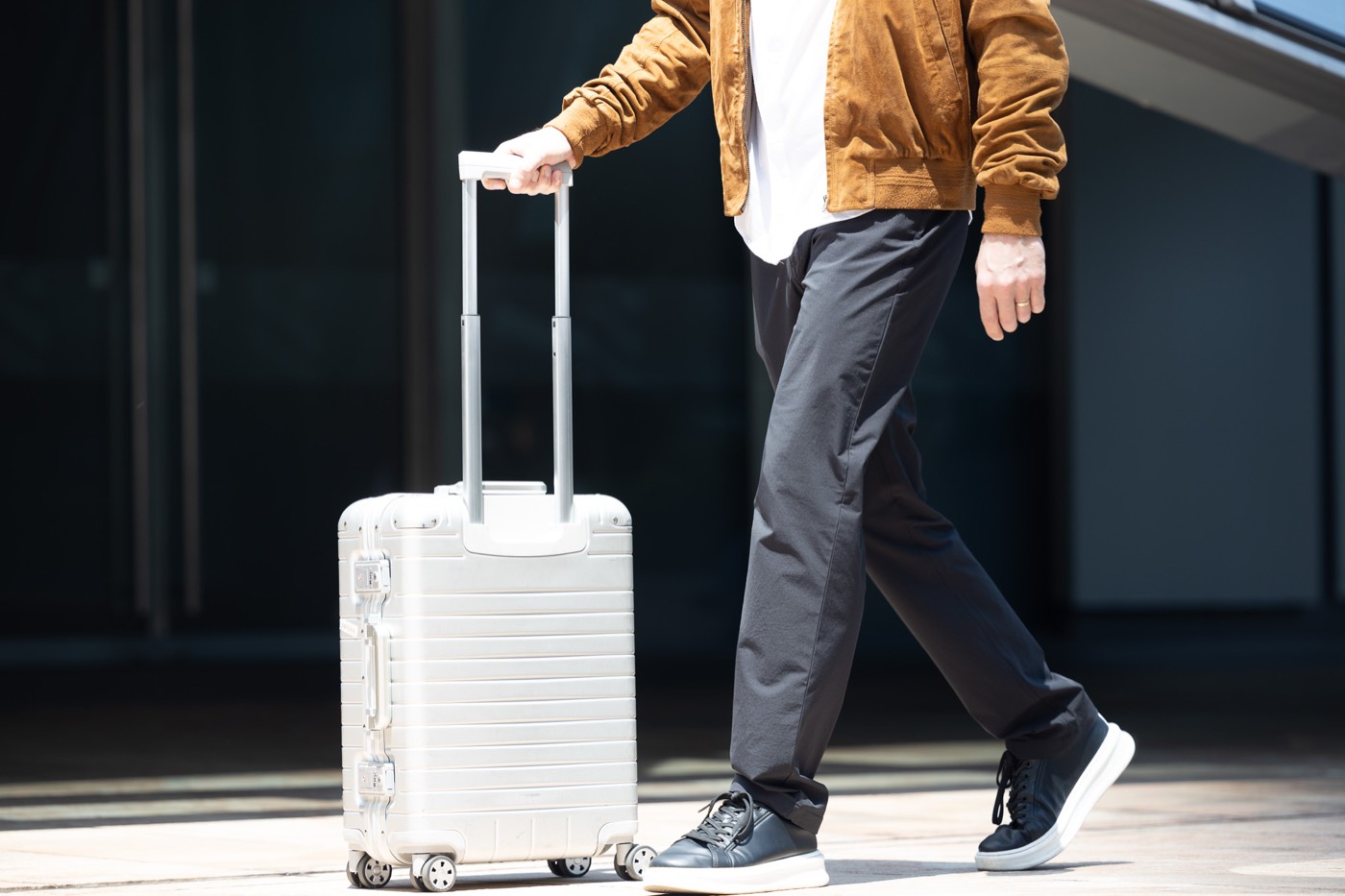 All Rounder Urban mid-stride beside an aluminum carry-on.